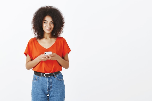 Mujer bonita con peinado afro posando con su teléfono inteligente en el estudio