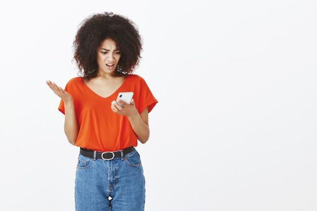 Mujer bonita con peinado afro posando con su teléfono inteligente en el estudio