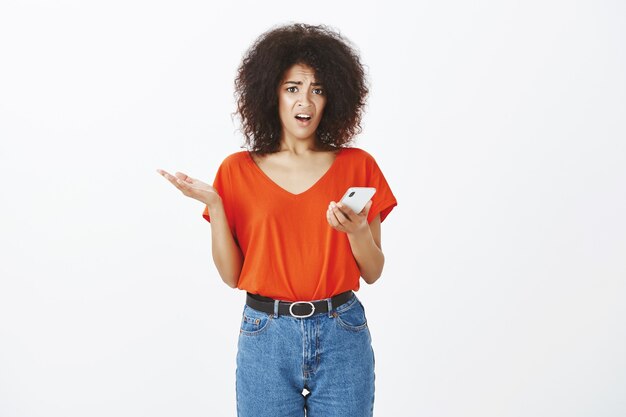 Mujer bonita con peinado afro posando con su teléfono inteligente en el estudio