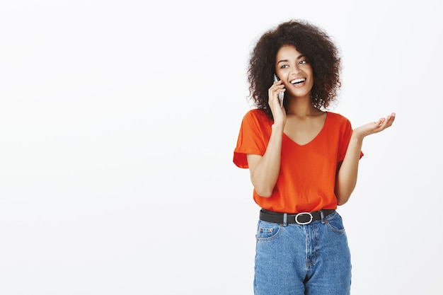 Mujer bonita con peinado afro posando con su teléfono inteligente en el estudio