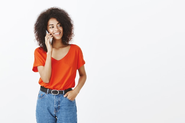 Mujer bonita con peinado afro posando con su teléfono inteligente en el estudio