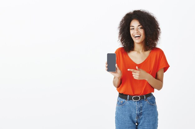 Mujer bonita con peinado afro posando con su teléfono inteligente en el estudio