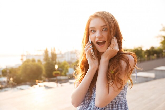 Mujer bonita pelirroja sorprendida con el pelo largo hablando por teléfono