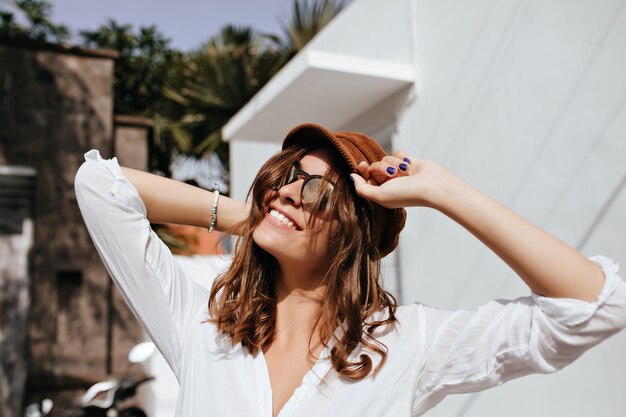 Mujer bonita de pelo corto sonríe sinceramente y disfruta del día soleado. Retrato de niña con gorra.