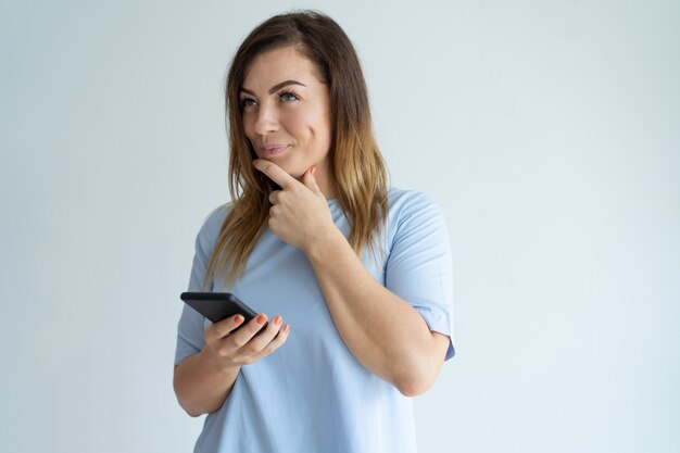 Mujer bonita pensativa que sostiene smartphone. Señora de mediana edad pensando.