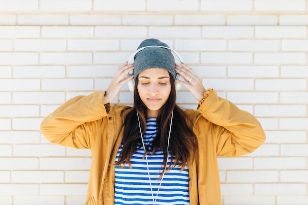 mujer bonita de pie contra la pared de ladrillo blanco con auriculares