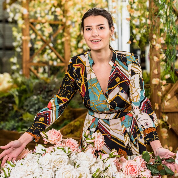 Mujer bonita que se coloca cerca de las flores color de rosa ligeras