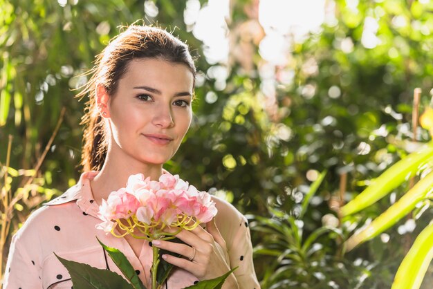 Mujer bonita que se coloca con la flor rosada a disposición