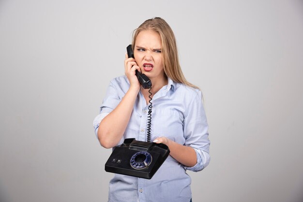 mujer bonita que sostiene el teléfono y que habla pared gris aislada.