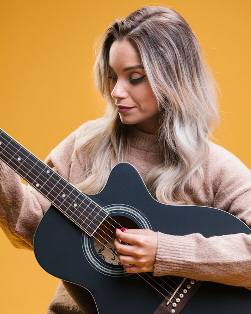 Mujer bonita que toca la guitarra contra fondo amarillo