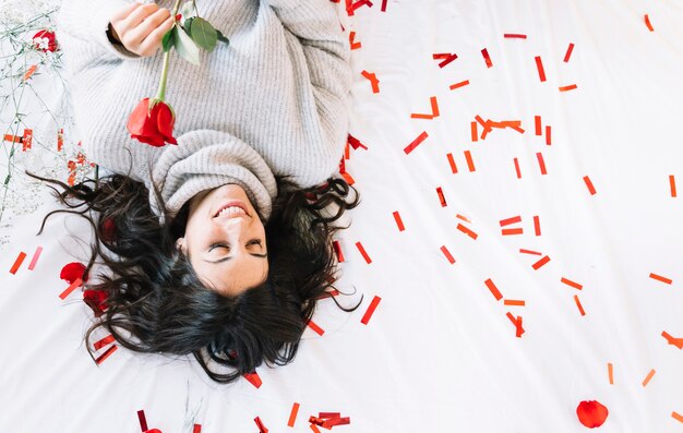 Mujer bonita con rosa acostado en confeti