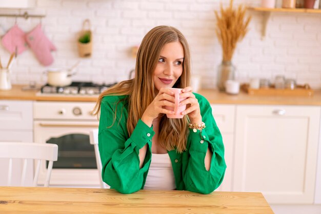 Mujer bonita rubia bebiendo té de café en su cocina, loungewear syulish brillante.