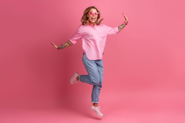 Mujer bonita rubia en camisa rosa y jeans sonriendo saltando