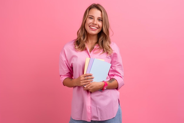 Mujer bonita rubia en camisa rosa sonriendo sosteniendo cuadernos de explotación