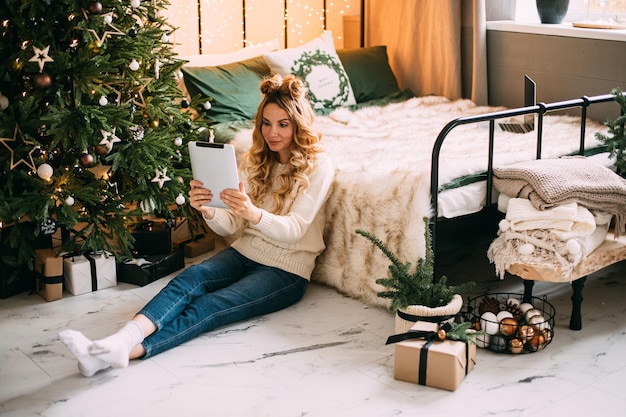 Mujer bonita rubia en casual usando tableta para llamar a sus amigos durante el encierro en Navidad.