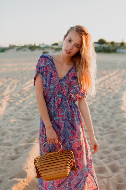 Mujer bonita rubia con ramo de lavanda caminando por la playa. Colores del atardecer.