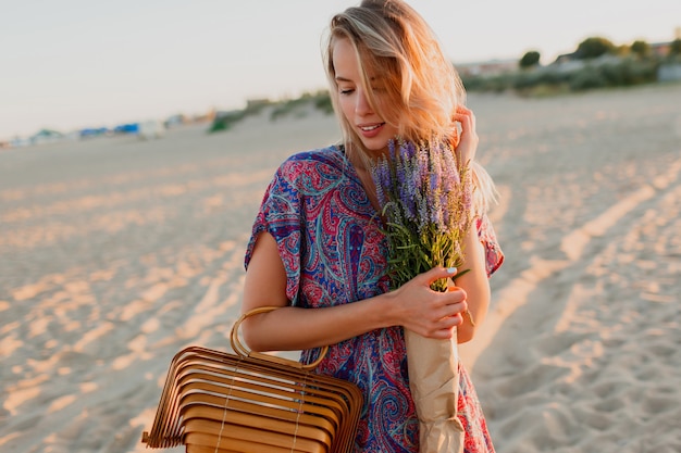 Mujer bonita rubia con ramo de lavanda caminando por la playa. Colores del atardecer.