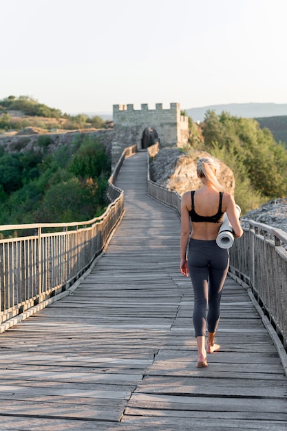 Mujer bonita rubia sosteniendo estera de yoga