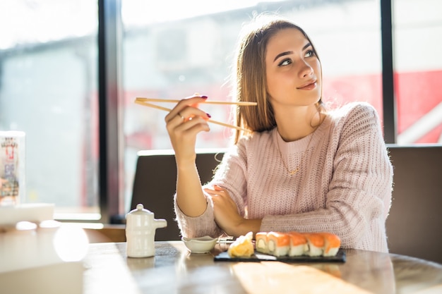 Mujer bonita rubia en suéter blanco comiendo sushi para el almuerzo en una pequeña cafetería