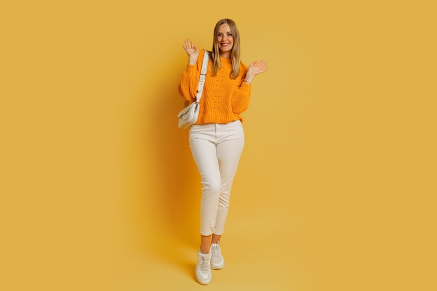 Mujer bonita rubia en traje de otoño de moda posando en amarillo. Sosteniendo el bolso de cuero blanco. De longitud completa.