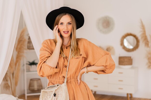 Mujer bonita rubia en vestido de lino beige posando en elegante boho intrerior.