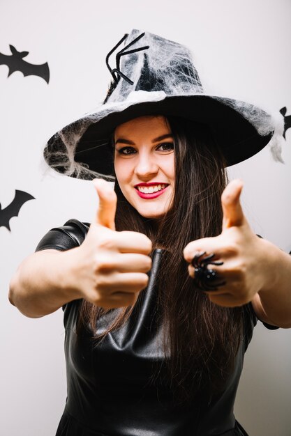 Mujer bonita en sombrero decorado que muestra los pulgares para arriba