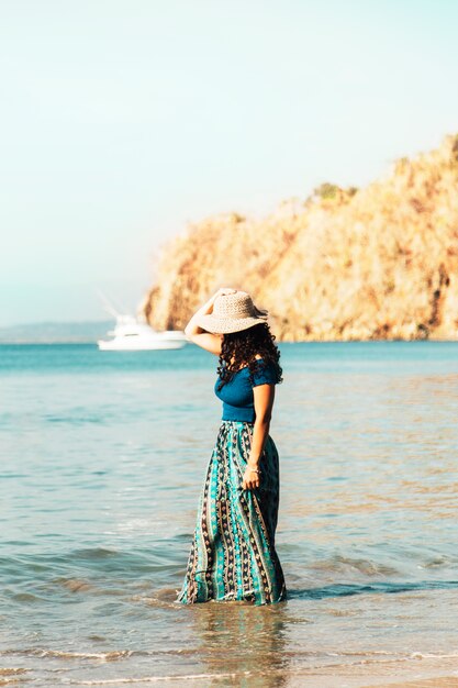 Mujer bonita en el sombrero que se coloca en onda costera en la playa