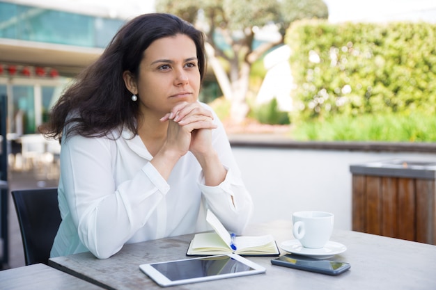 Mujer bonita soñadora que se relaja y que se sienta en café de la calle