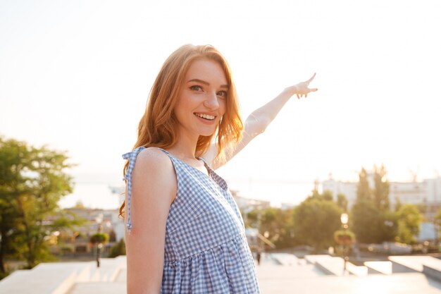 Mujer bonita sonriente que señala el dedo lejos mientras está de pie al aire libre