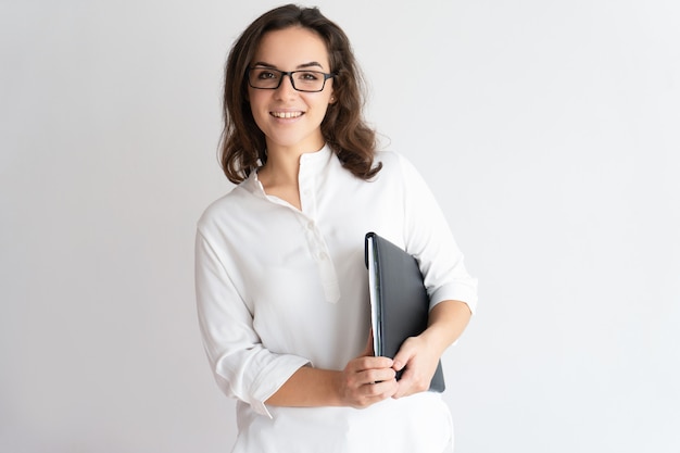 Mujer bonita sonriente que sostiene el archivo debajo de su axila y que mira la cámara.