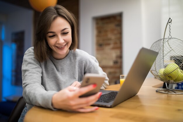 Mujer bonita sonriente que trabaja en casa en una computadora de computadora portátil