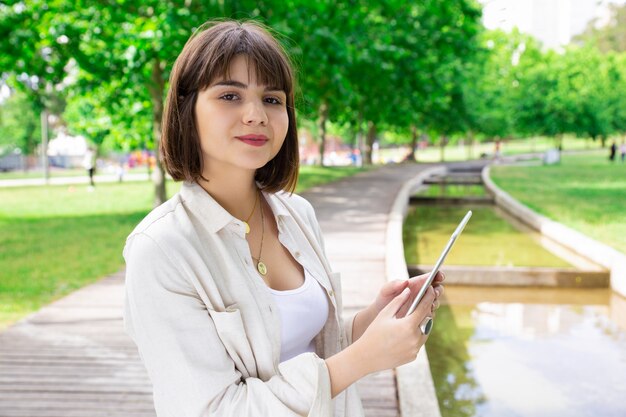 Mujer bonita sonriente que usa la tableta en parque