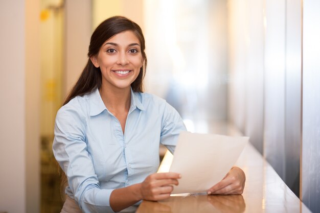 Mujer bonita sonriente de sujeción de documentos en el Café