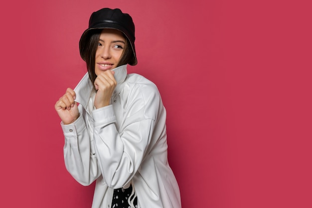 Mujer bonita con sonrisa perfecta vestida con elegante gorra y chaqueta blanca posando sobre fondo rosa. Aislar.