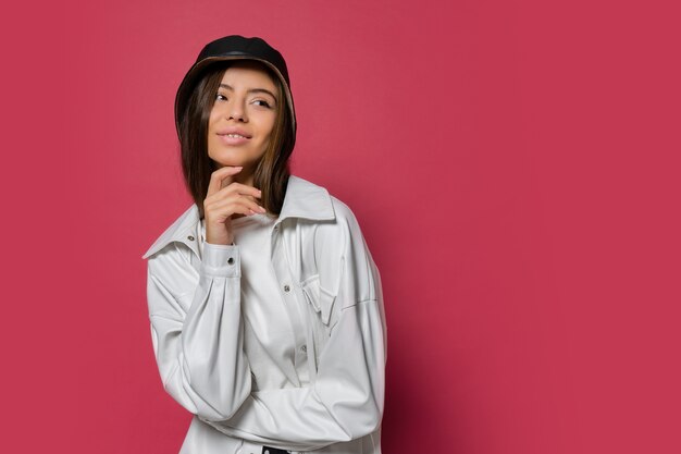 Mujer bonita con sonrisa perfecta vestida con elegante gorra y chaqueta blanca posando sobre fondo rosa. Aislar.