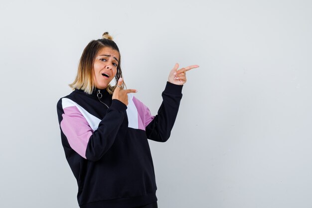 Mujer bonita en sudadera apuntando hacia el lado derecho, abriendo la boca y mirando sorprendido