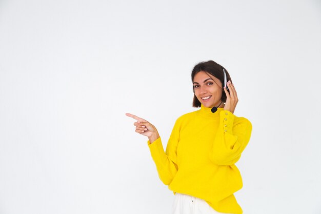 Mujer bonita en suéter amarillo sobre blanco gerente con auriculares sonrisa feliz señalar con el dedo a la izquierda