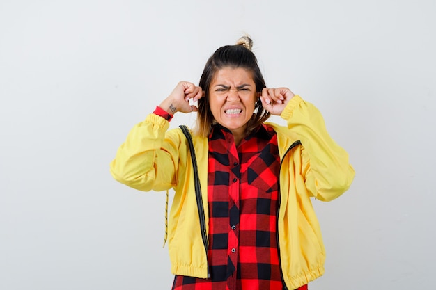 Mujer bonita tapando los oídos con los dedos en camisa, chaqueta y mirando molesto, vista frontal.