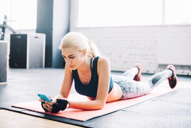 Mujer bonita con teléfono inteligente en el gimnasio