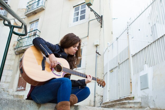 Mujer bonita tocando la guitarra en las escaleras de la calle