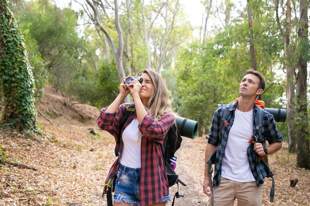 Mujer bonita tomando fotos de paisaje con cámara y viajando con novio. Turistas caucásicos caminando juntos. Mochilero macho mirando el paisaje. Concepto de turismo, aventura y vacaciones de verano.