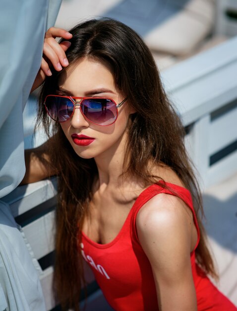 Mujer bonita en traje de baño rojo se sienta en sofá blanco fuera