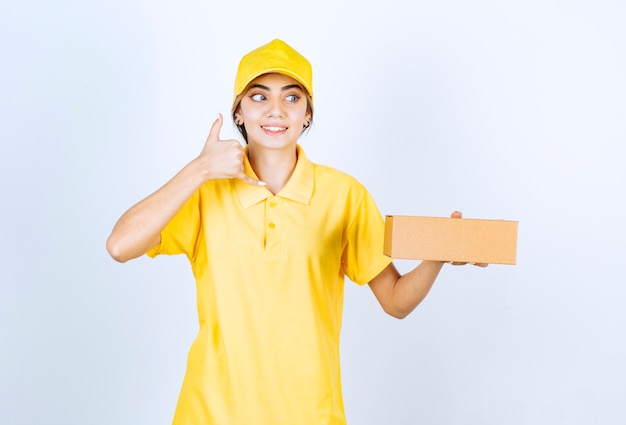 Una mujer bonita en uniforme amarillo con una caja de papel artesanal en blanco marrón que hace el distintivo de llamada.