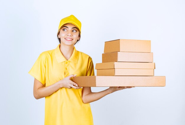 Una mujer bonita en uniforme amarillo con cajas de papel artesanal marrón en blanco.