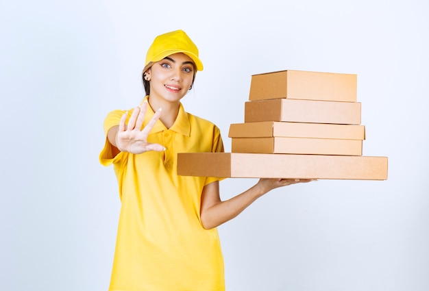 Una mujer bonita en uniforme amarillo con cajas de papel artesanal marrón en blanco.