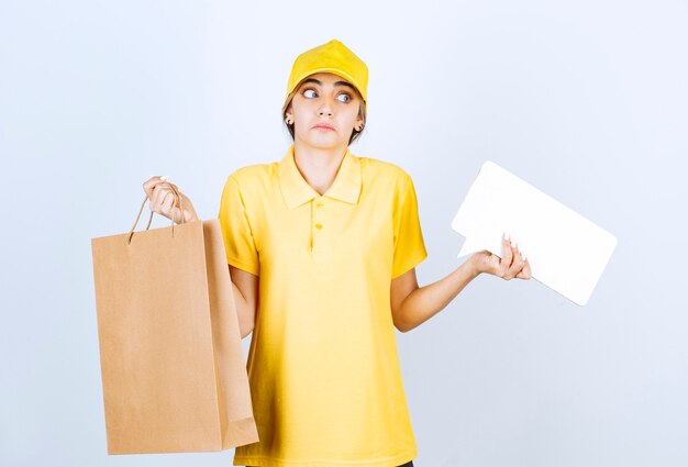 Una mujer bonita en uniforme amarillo sosteniendo una bolsa de papel artesanal en blanco marrón y un bocadillo en blanco.