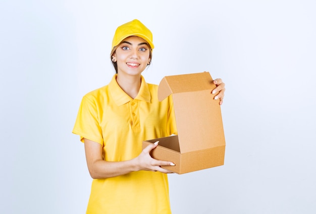 Una mujer bonita en uniforme amarillo sosteniendo una caja de papel artesanal en blanco marrón abierta.