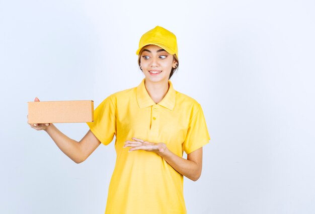 Una mujer bonita en uniforme amarillo sosteniendo una caja de papel artesanal marrón en blanco.