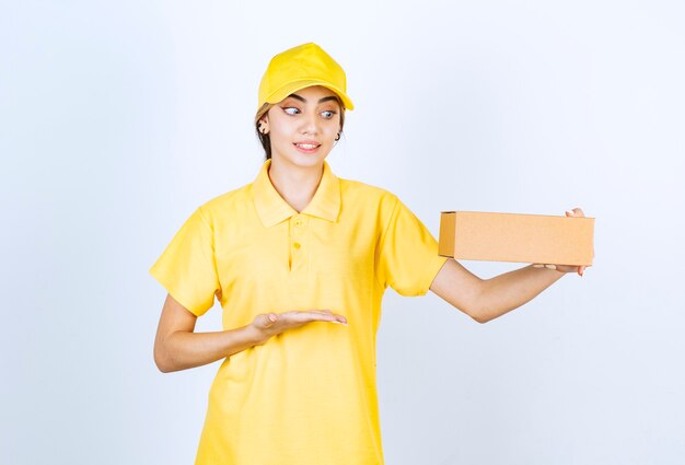 Una mujer bonita en uniforme amarillo sosteniendo una caja de papel artesanal marrón en blanco.