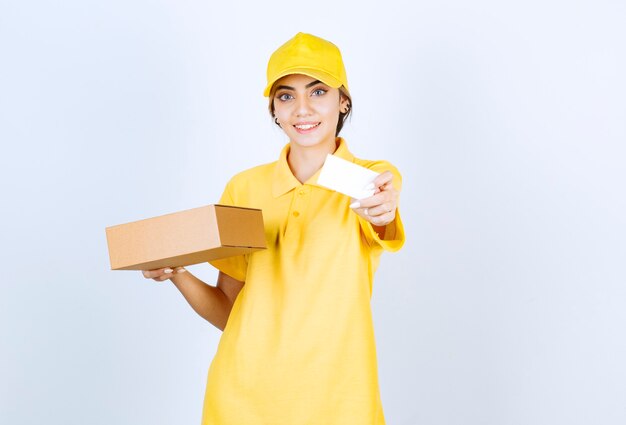 Una mujer bonita en uniforme amarillo sosteniendo una caja de papel artesanal marrón en blanco.